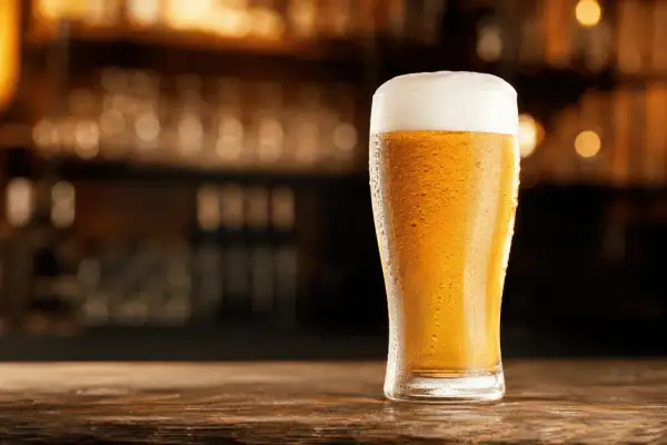 Chłodne pils piwo z obfitą pianką, skraplające się od orzeźwienia, stoi na drewnianym blacie.