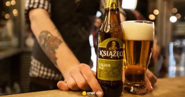 Ręka z tatuażem sięga po butelkę piwa Książęce Golden Ale. Czy to piwo jest gorzkie?