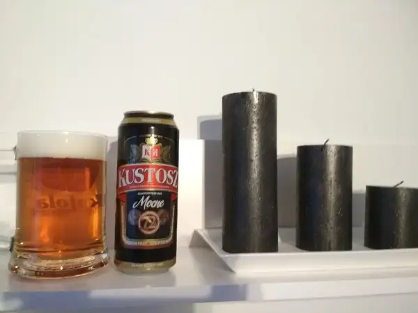 Kufel piwa i puszka Kustosz Mocne obok trzech czarnych świec.