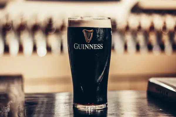 Szklanka ciemnego piwa stout Guinness z pianką na wierzchu, na drewnianym blacie.