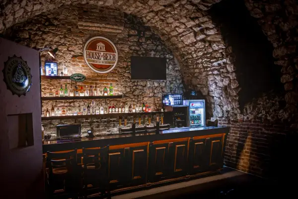 Wnętrze "House of Beer" z kamiennymi ścianami, barem pełnym butelek i kranów piwnych.