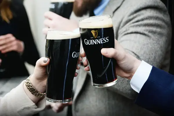 Dwie osoby wznoszą toast szklankami ciemnego piwa Guinness. Zastanawiasz się, ile procent alkoholu ma Guinness?