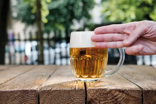 Dłoń dotyka gęstej piany na kuflu piwa, pokazując, jak powstaje piana.